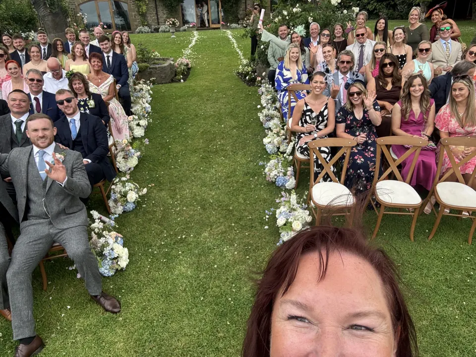 Sarah taking a crowd selfie at an outdoor wedding